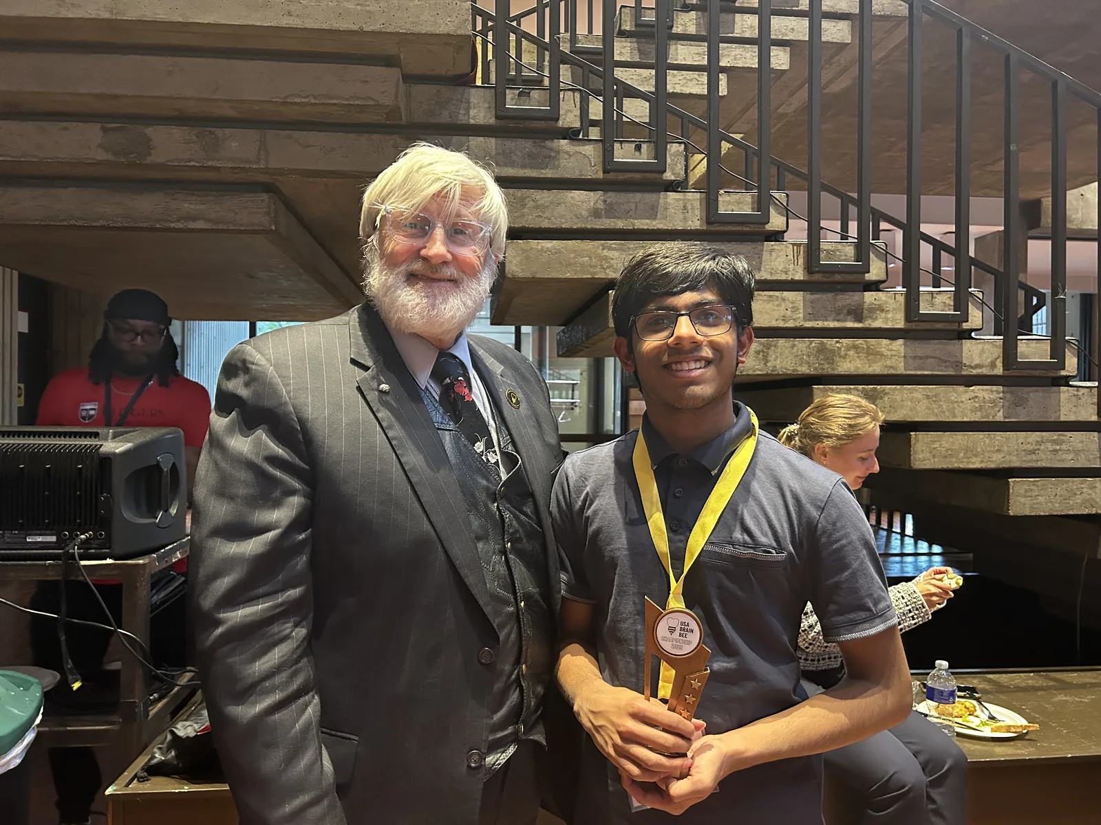 Navneeth Badhri holding the USA Brain Bee trophy at the national finals, standing next to the competition's organiser.